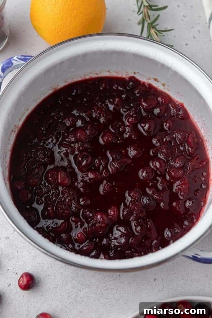Close-up of cranberry sauce cooking in a pot on the stove, showing cranberries bursting.