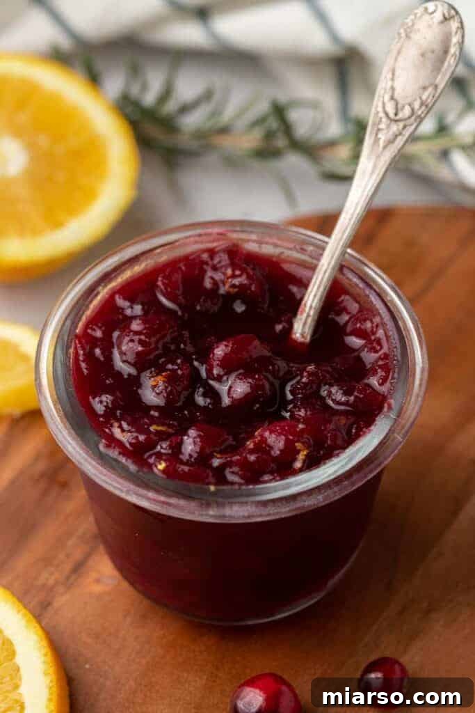 Homemade cranberry sauce with oranges in a canning jar, garnished with a sprig of rosemary.