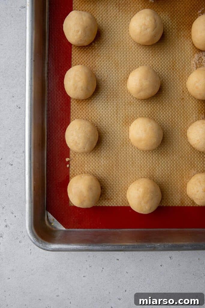 Golden Oreo Cheesecake Truffles 6 Rolled truffle balls chilling on a baking sheet lined with parchment paper.