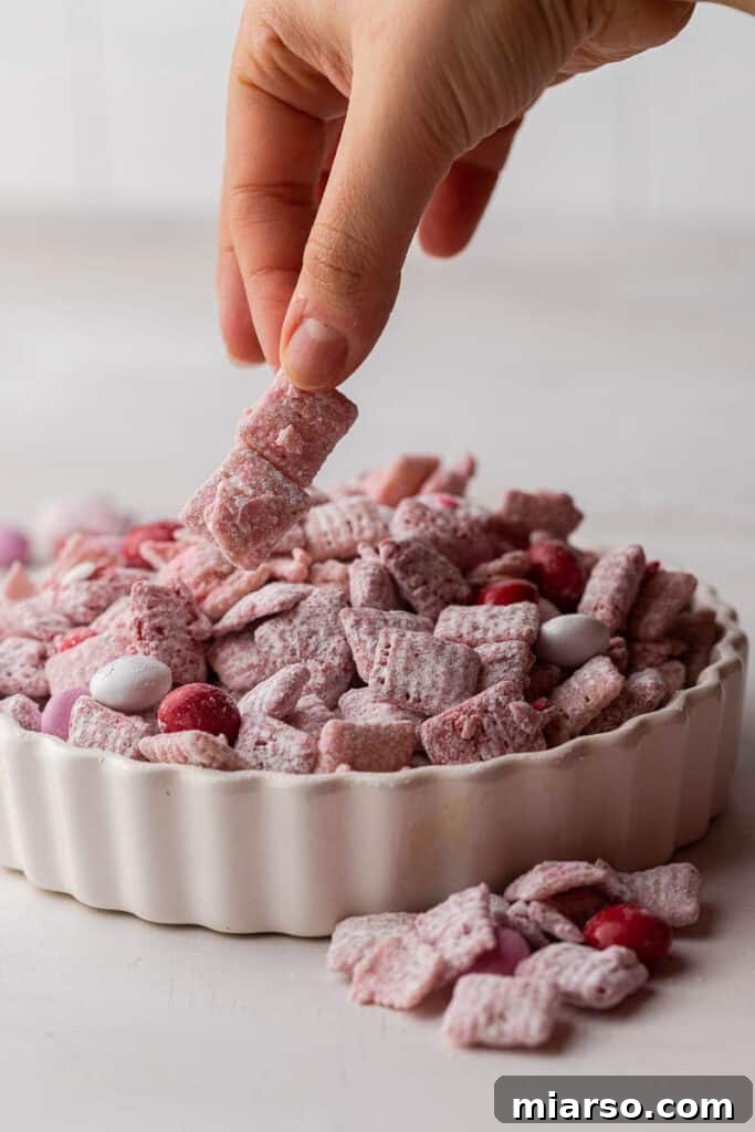 Cupid's Crunch 15 A hand reaching into a bowl of Valentine's Day muddy buddies, ready to grab a handful.