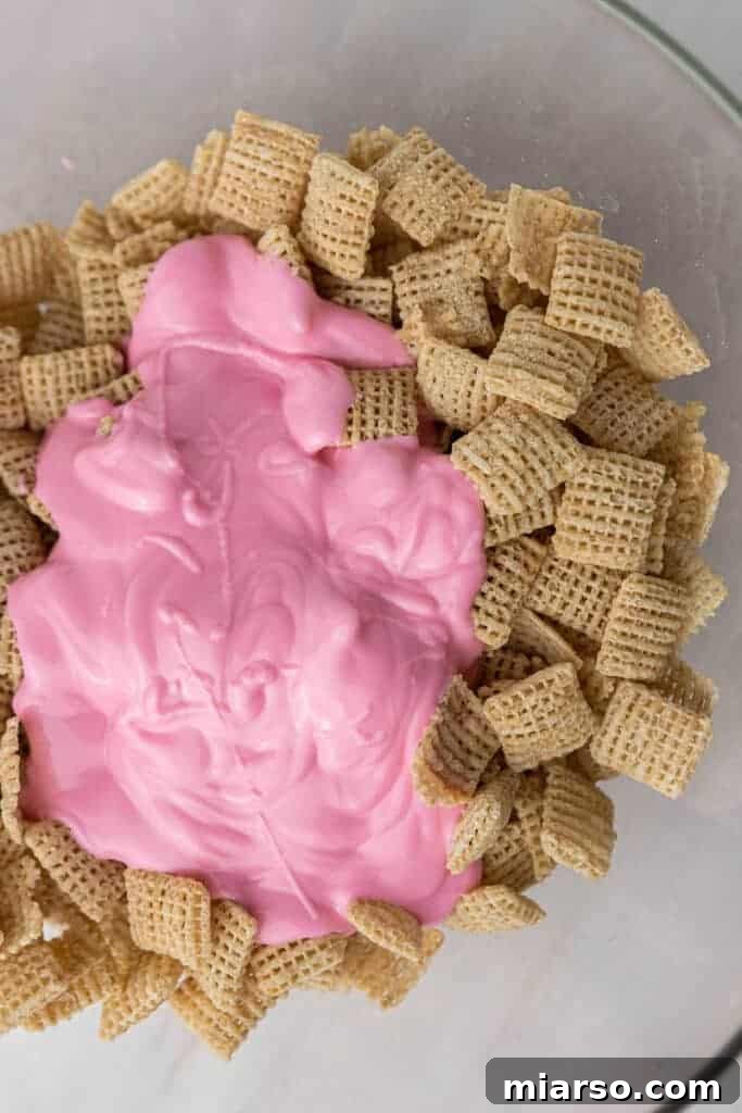 Cupid's Crunch 5 Chex cereal being coated with vibrant pink candy melts in a mixing bowl.