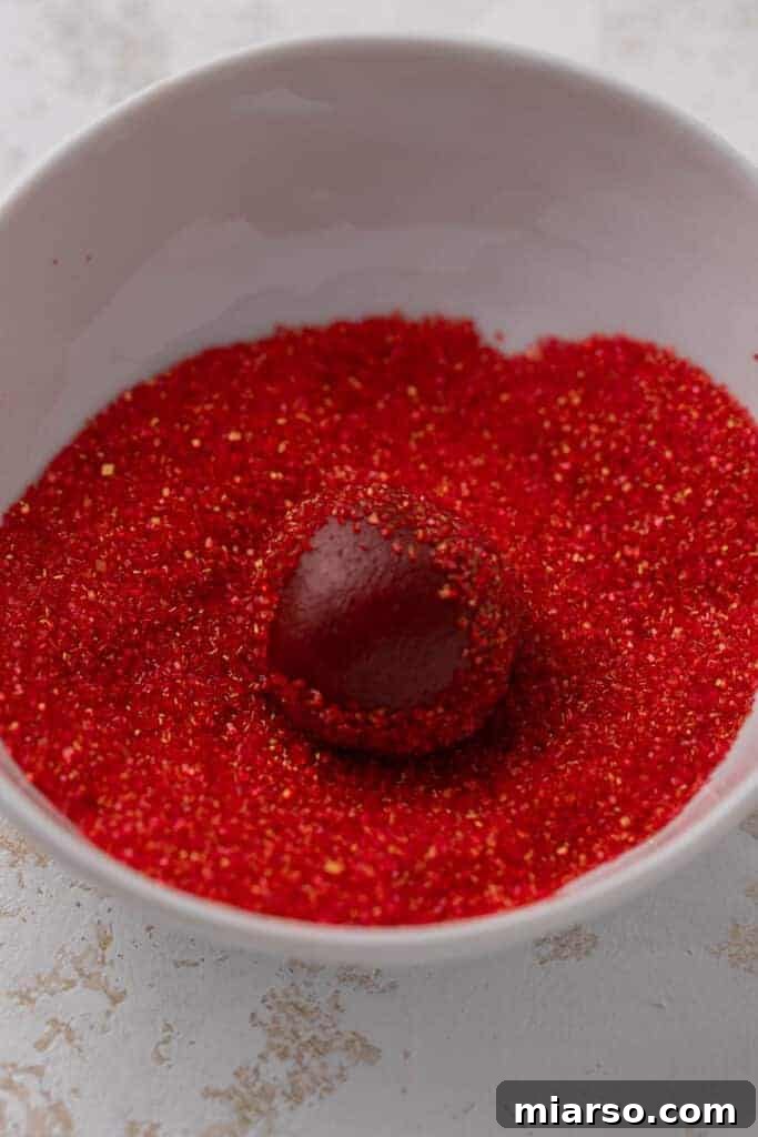 Hershey's Kissed Red Velvet Cookies 7 Red velvet cookie dough being rolled in sparkling red sugar, ready for baking