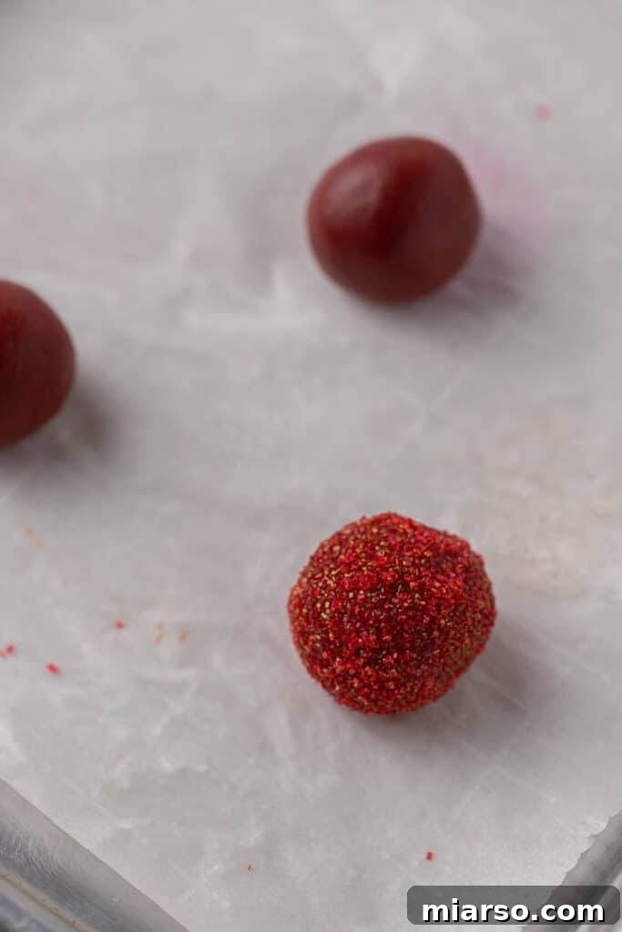Hershey's Kissed Red Velvet Cookies 8 Red velvet cookie dough balls coated in red sugar, neatly arranged on a baking sheet