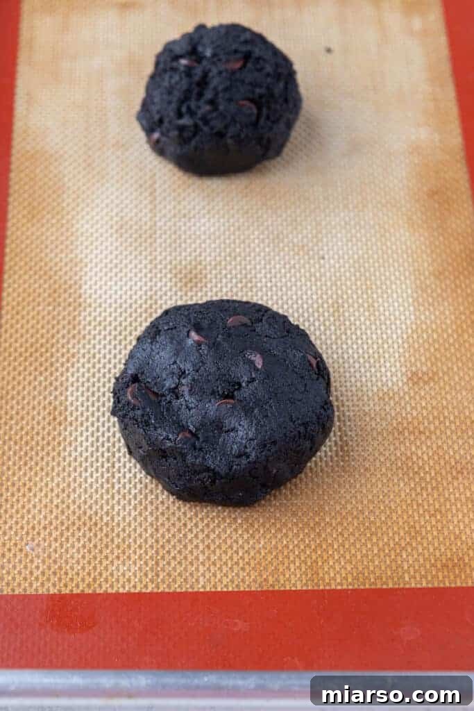 Step 3: Scooped and gently flattened dark chocolate cookie dough balls on a parchment-lined baking sheet.