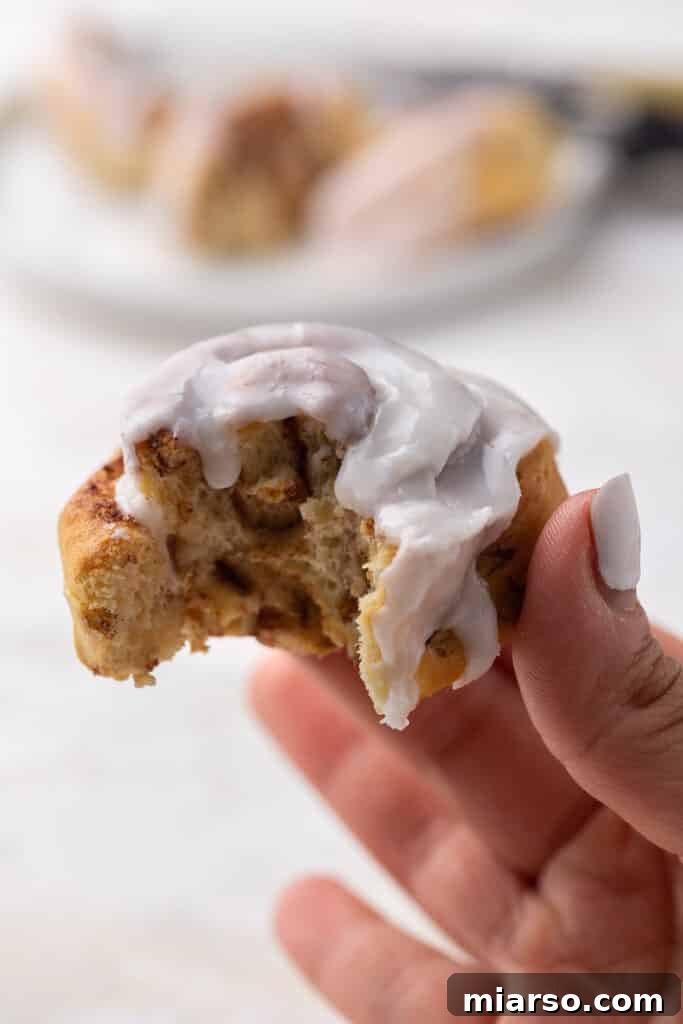 A hand holding a perfectly air-fried cinnamon roll, showing its golden exterior and soft interior.
