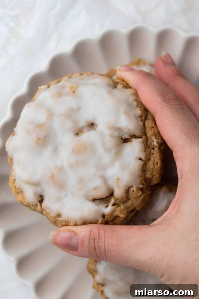 A hand holding a beautifully iced oatmeal cookie, highlighting its perfect shape and glaze.