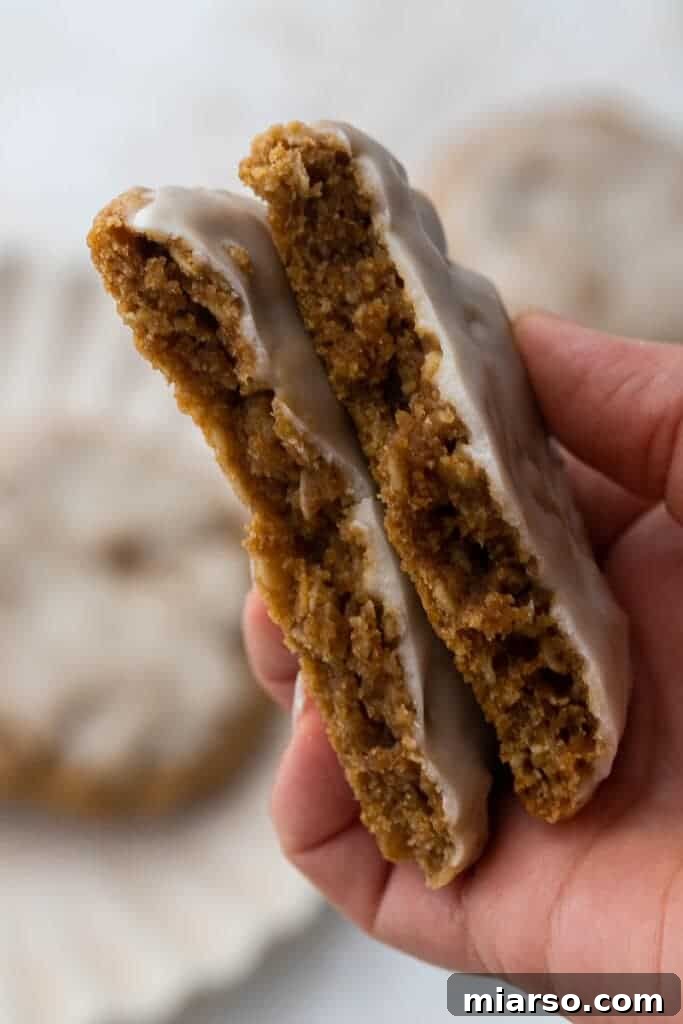 A hand gently holding a freshly iced oatmeal cookie, showcasing its perfect glaze.