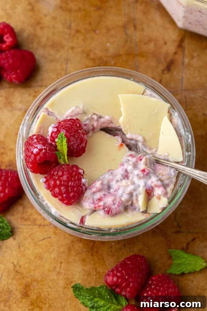 Raspberry overnight oats in a glass jar, showing layers of pink oats and a white chocolate topping.