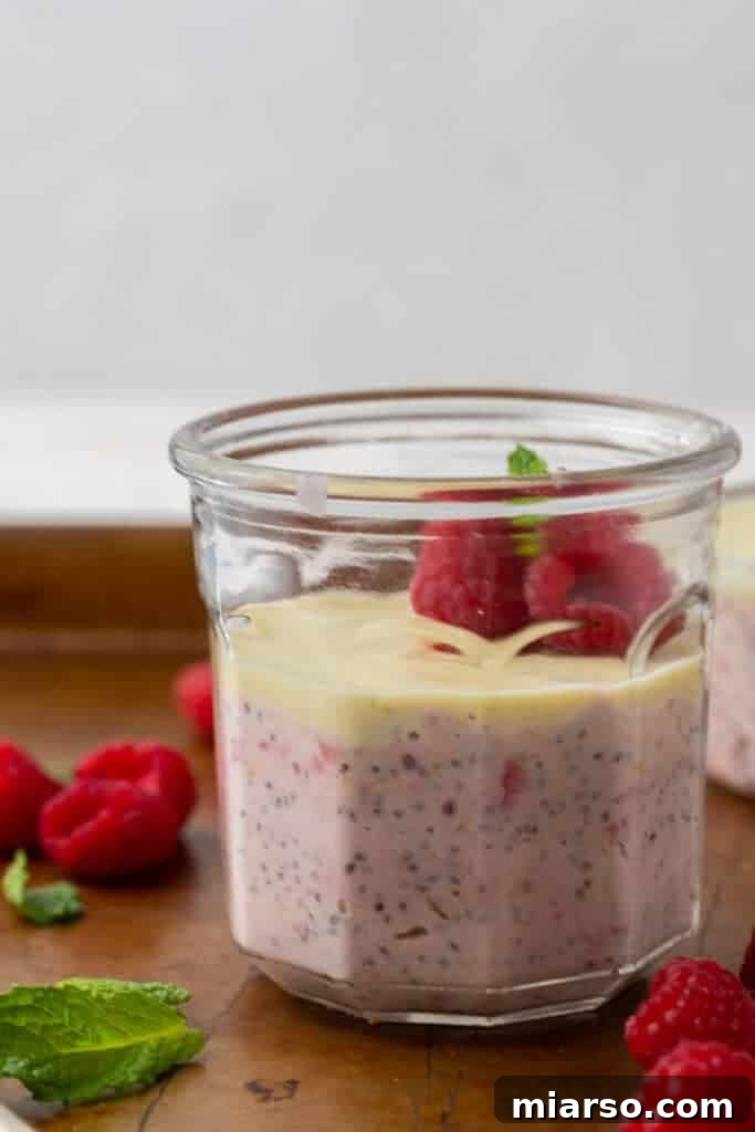 Layered white chocolate raspberry overnight oats in a clear cup, showing distinct layers of pink oats and white chocolate.