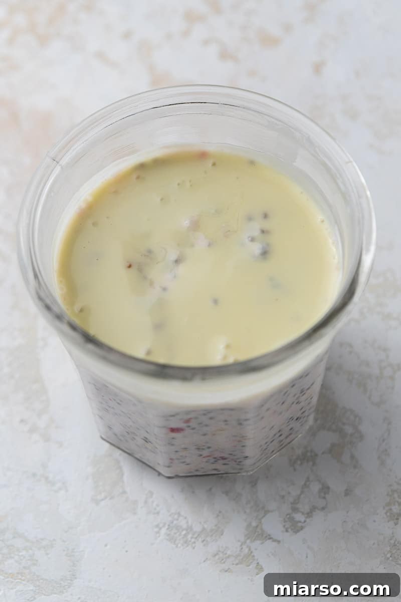 Melted white chocolate being poured over overnight oats in a cup.