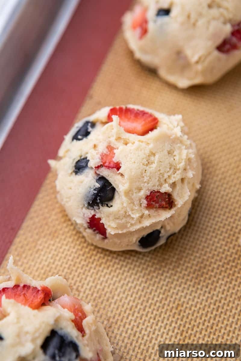Cookie dough with fresh blueberries and strawberries on a baking sheet