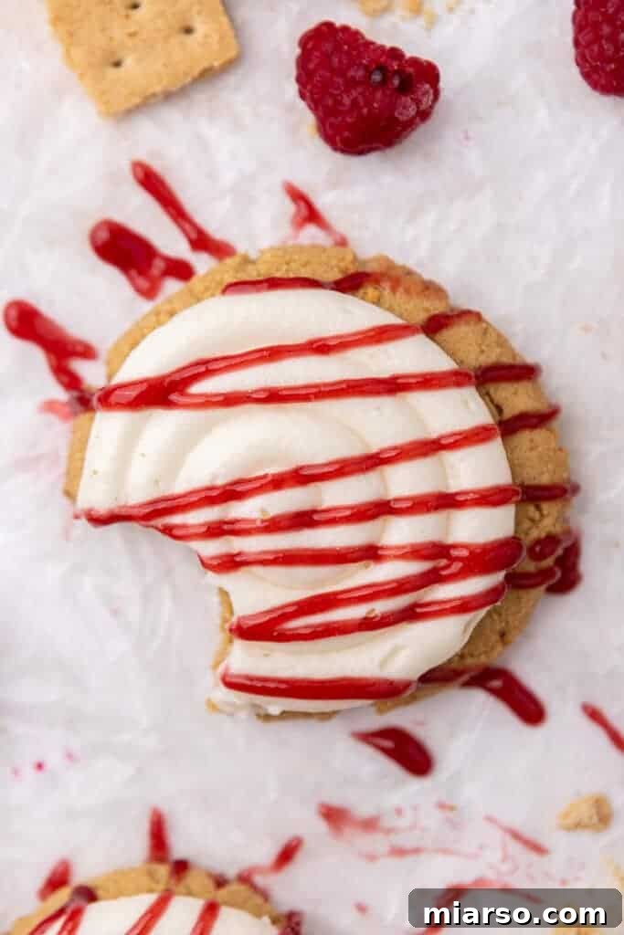 Indulgent Crumbl Raspberry Cheesecake Cookie on a pristine white background, showcasing its thick graham cracker base, creamy frosting, and vibrant raspberry swirl.
