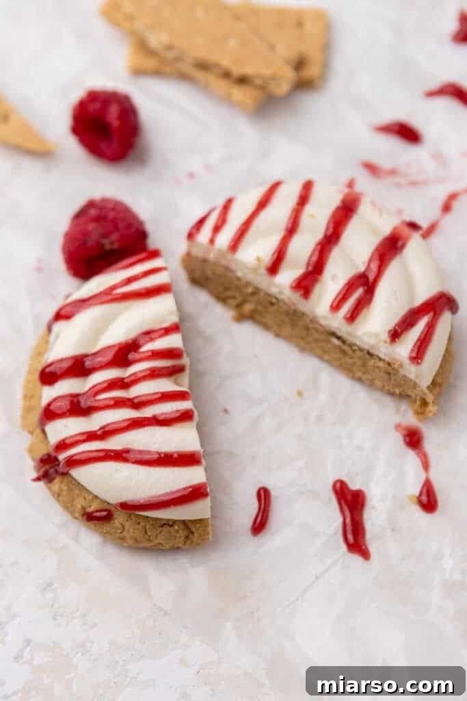 A Crumbl Raspberry Cheesecake Cookie sliced in half, revealing its thick graham cracker base and layers of creamy frosting and raspberry jam.