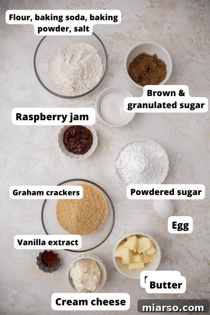Close-up of essential ingredients for Raspberry Cheesecake Cookies laid out on a wooden surface, including butter, sugars, eggs, flour, graham crackers, cream cheese, and raspberry jam.