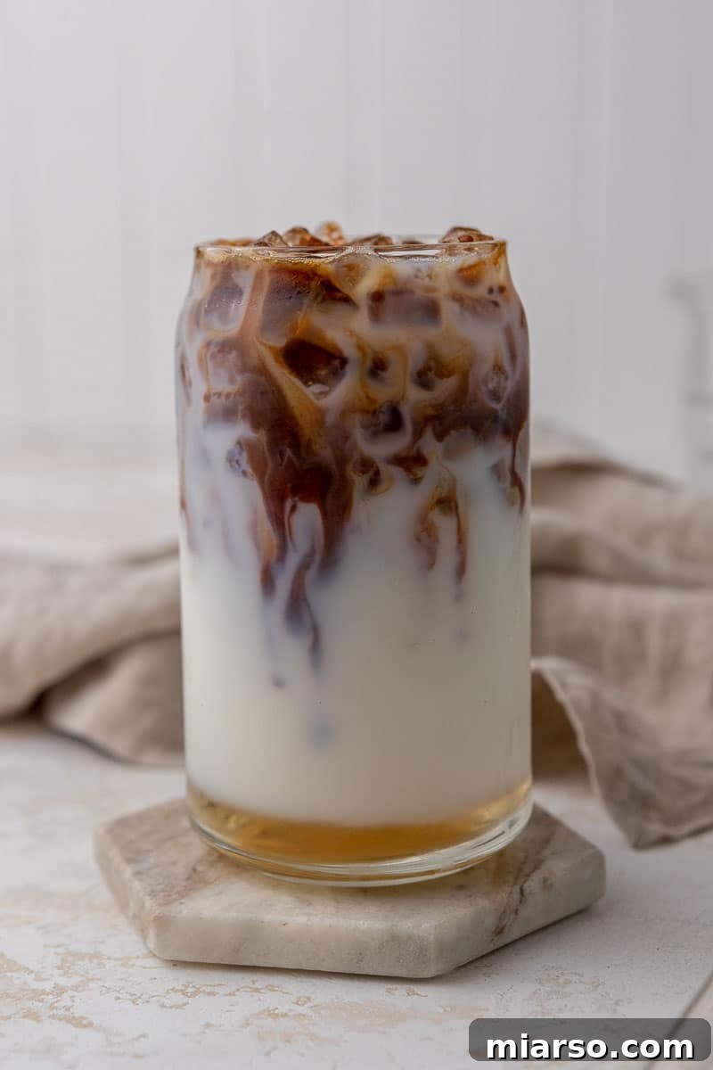 Starbucks Inspired Homemade Iced Caramel Macchiato 5 Espresso being gently poured into a glass with milk and vanilla syrup, creating a layered effect.