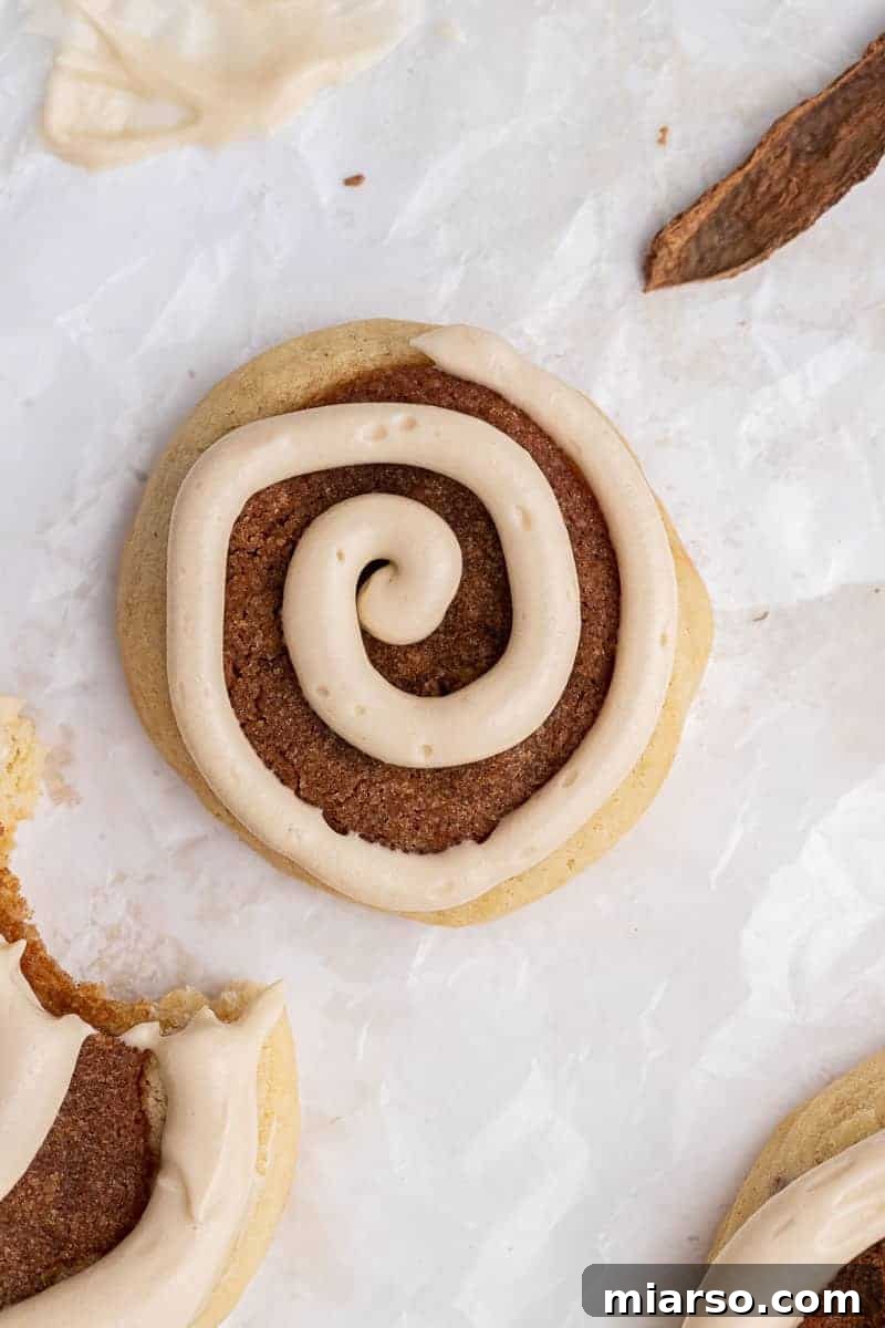 Maple cream cheese frosting being piped onto a warm cinnamon roll cookie