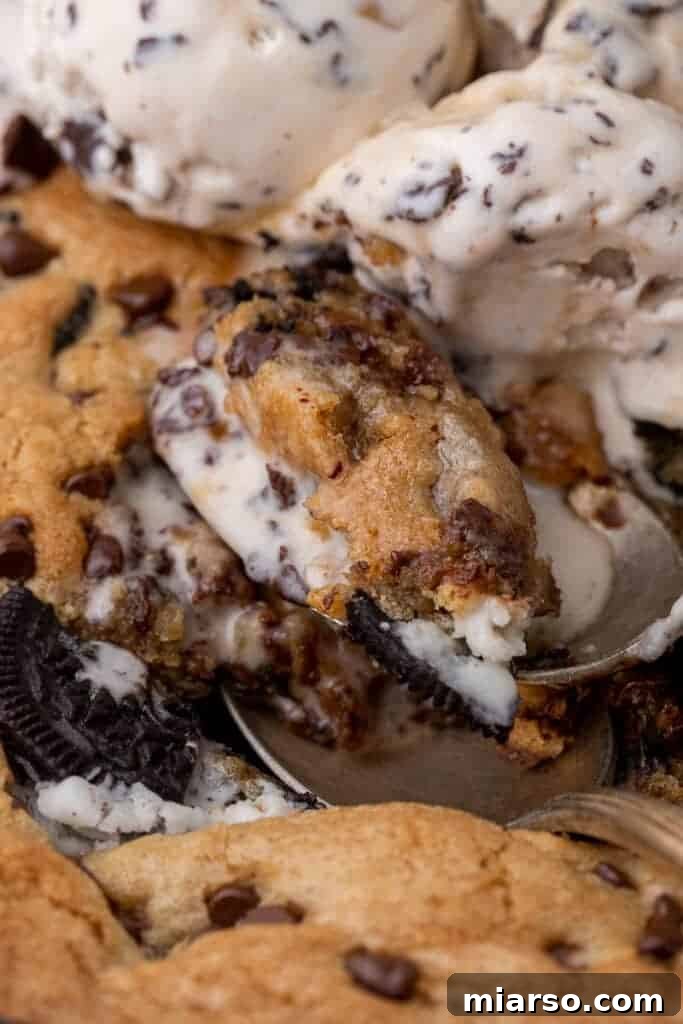 Effortless Giant Oreo Skillet Cookie 2 Close up of a warm cookies and cream skillet cookie topped with melting ice cream and a spoon digging in.