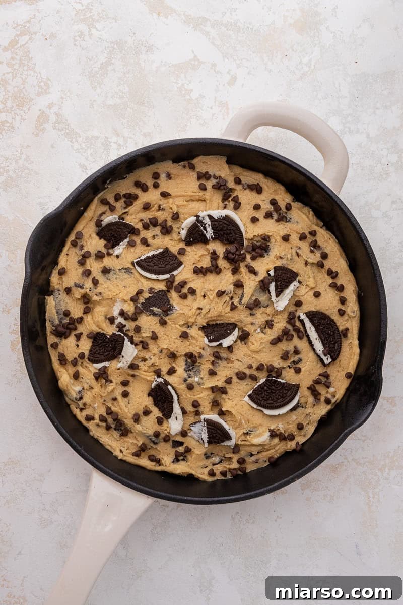 Effortless Giant Oreo Skillet Cookie 6 Cookie dough spread evenly in a cast iron skillet before baking, with extra toppings.