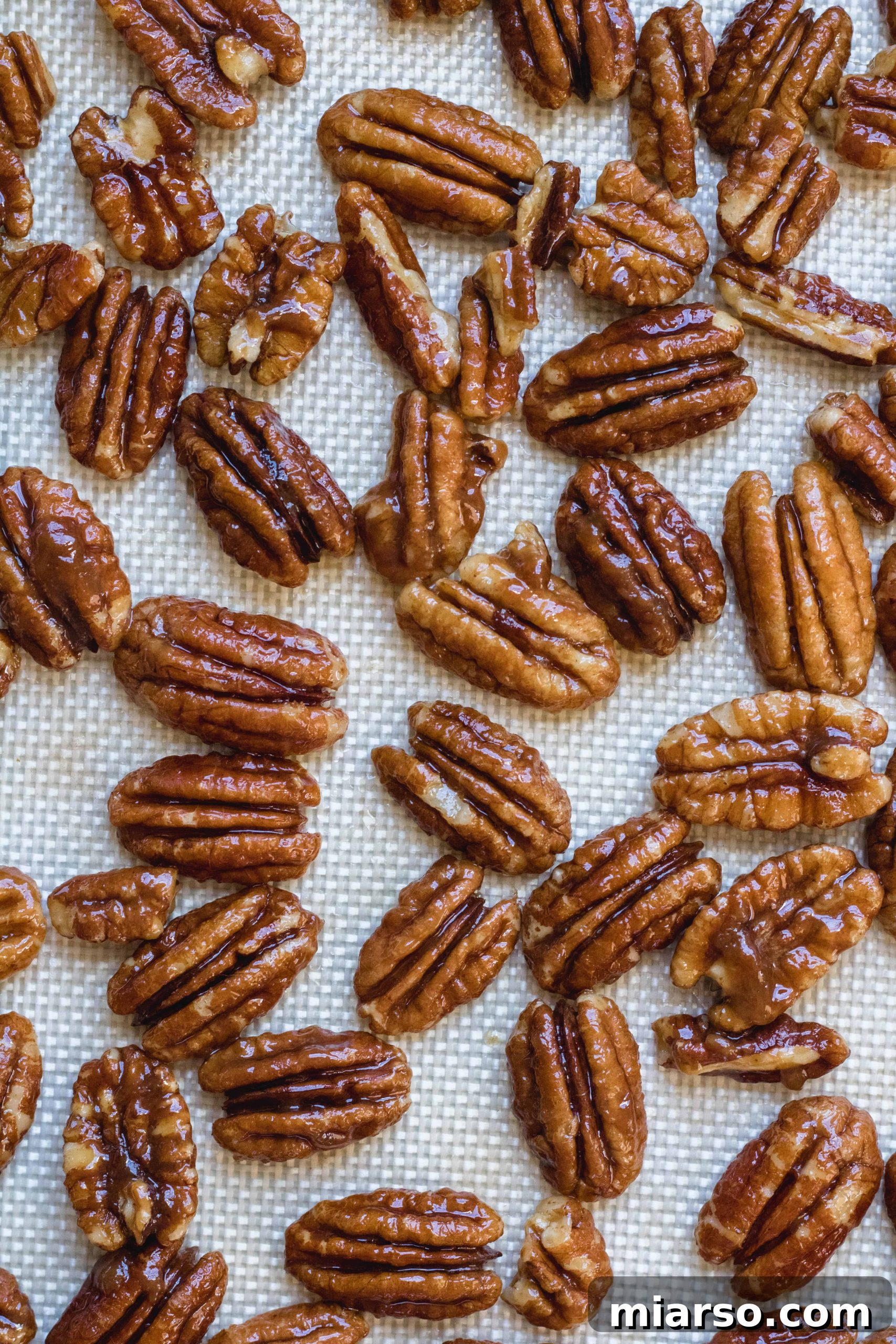 Candied pecans spread evenly on parchment paper, sprinkled with sea salt.