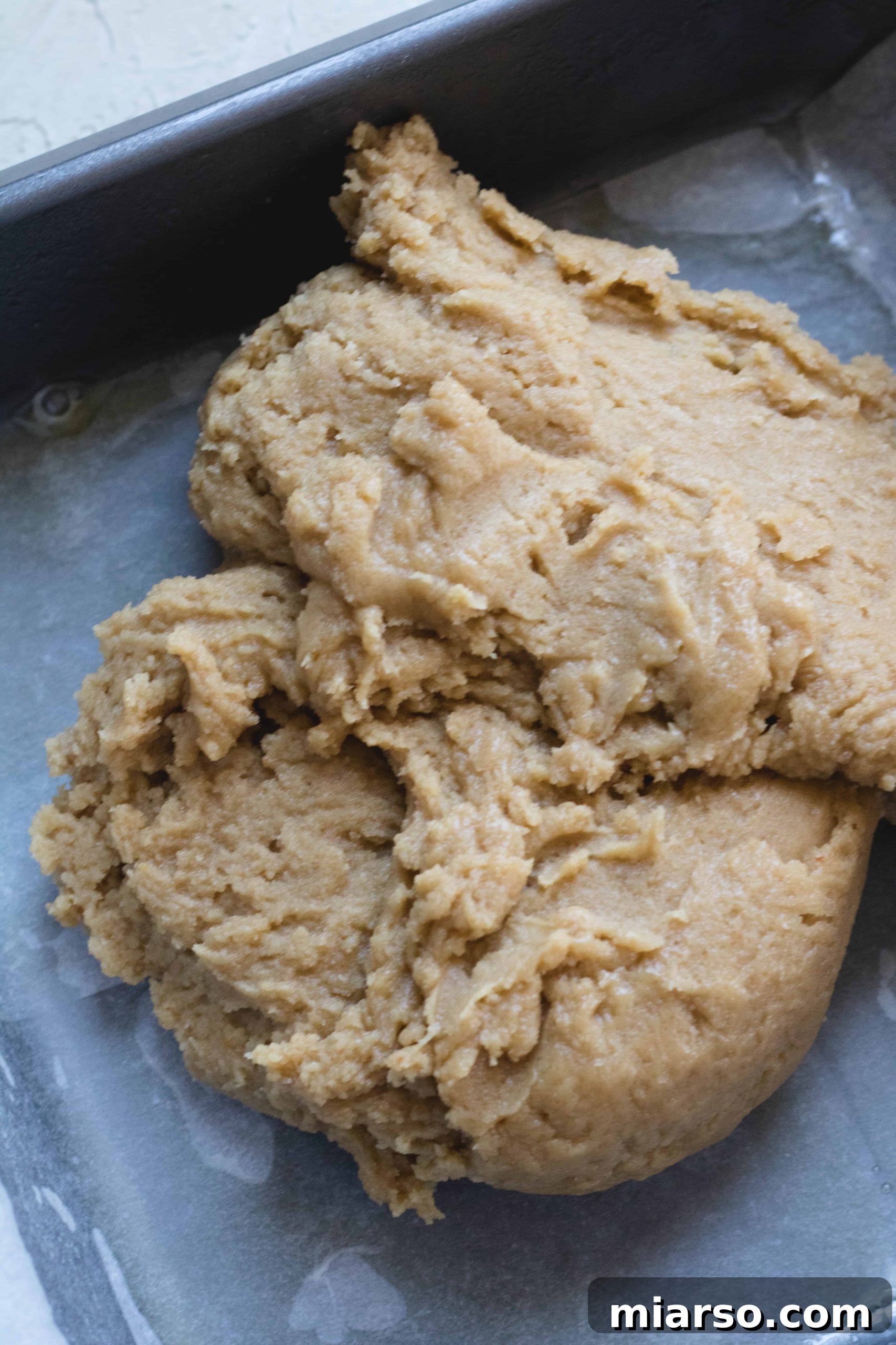 Brown butter blondie dough being pressed into a prepared baking pan.