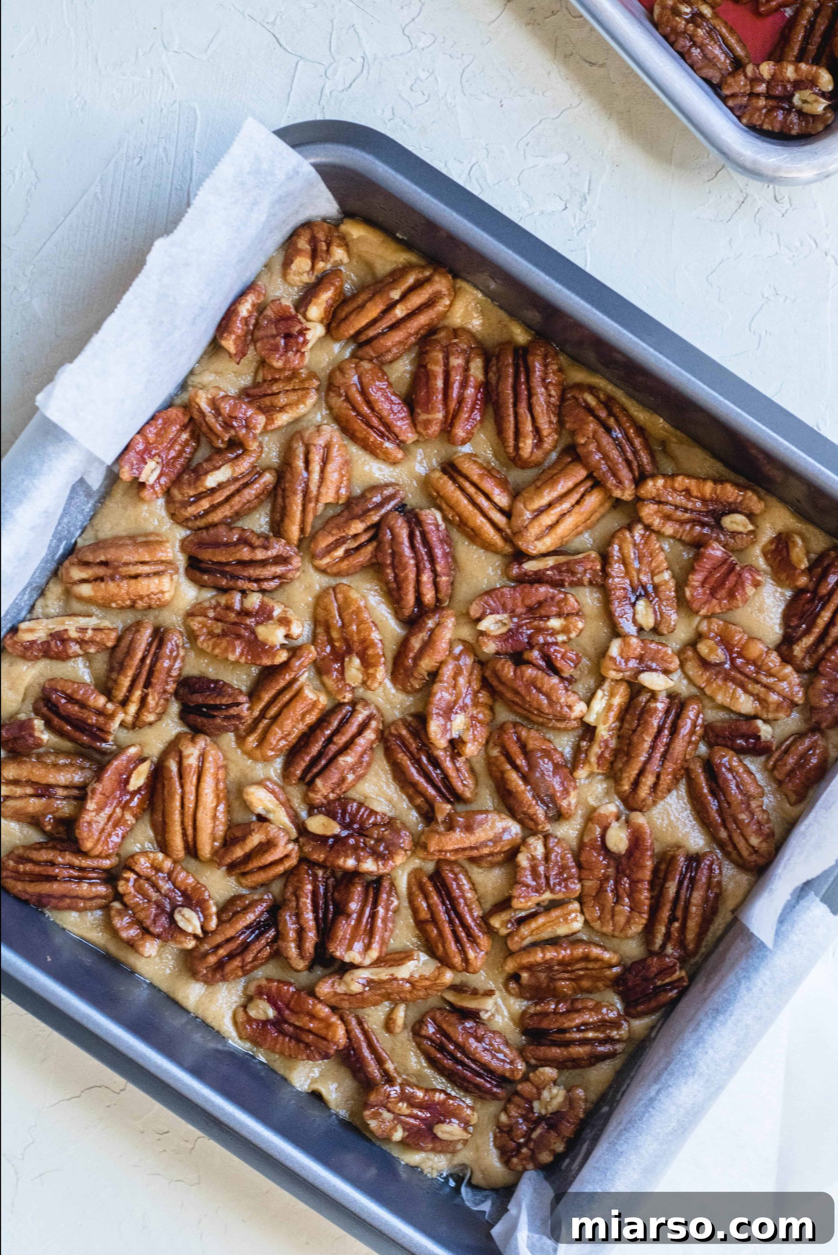 Brown butter blondie dough generously topped with candied pecans before baking.