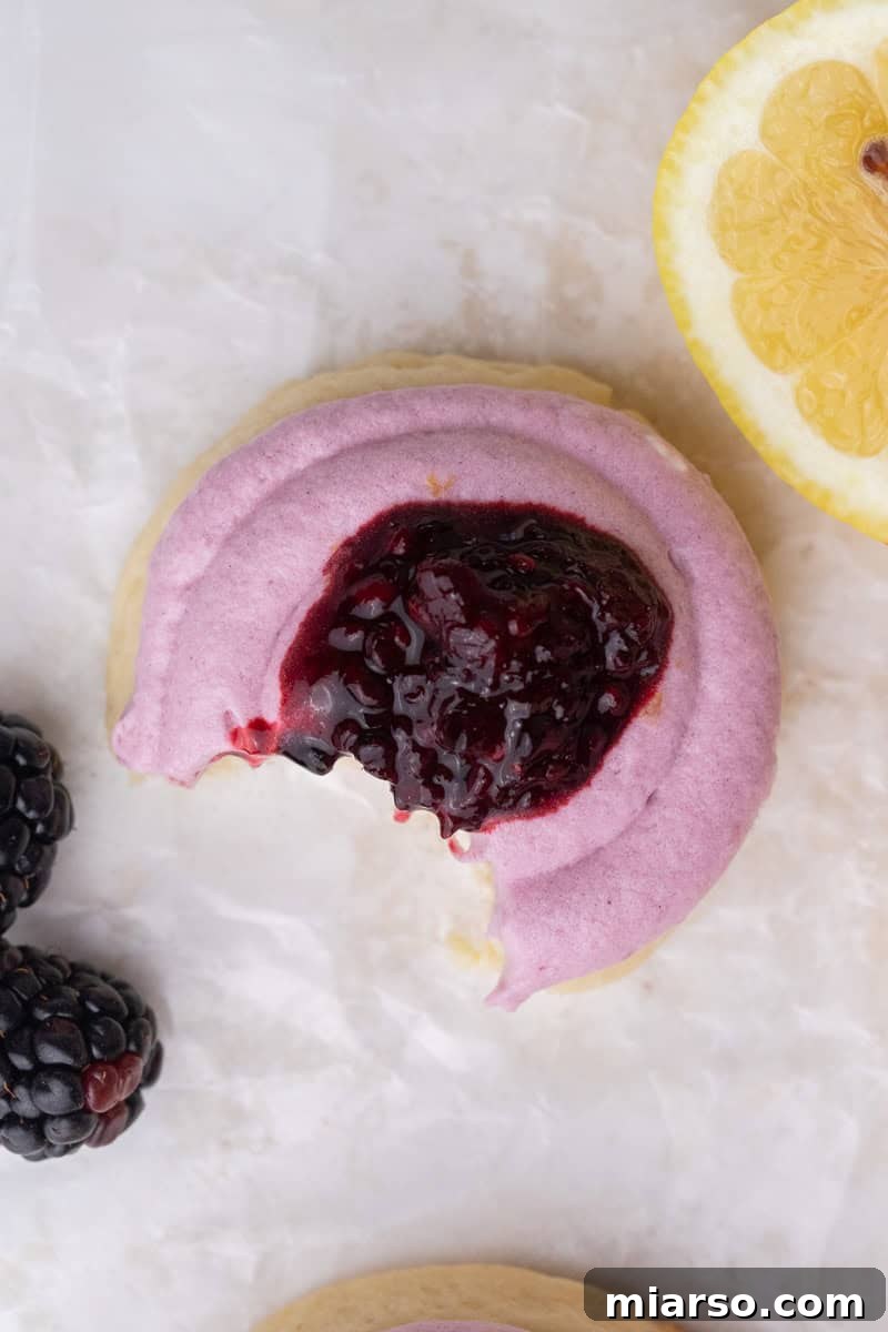 A freshly baked Crumbl lemon blackberry cookie with a bite taken out, showing the soft interior and frosting