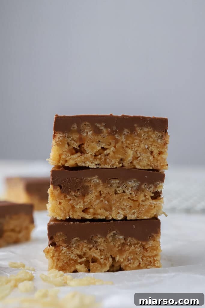 A stack of three soft Scotcheroos on a rustic wooden surface, highlighting their delicious layers.