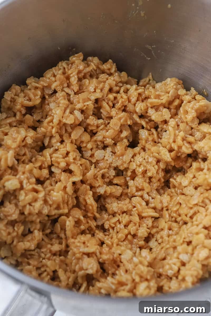 Crispy rice cereal being added to the peanut butter mixture in a large bowl.