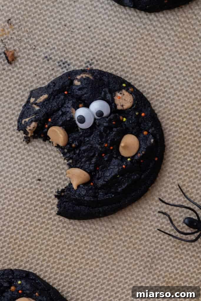 A plate of spooky black monster cookies with edible eyeballs and sprinkles.