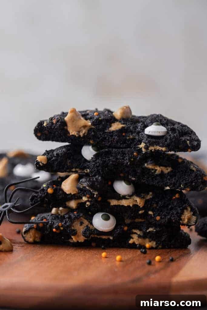 A stack of delicious black Halloween monster cookies, adorned with colorful sprinkles and edible eyeballs, ready to be enjoyed.