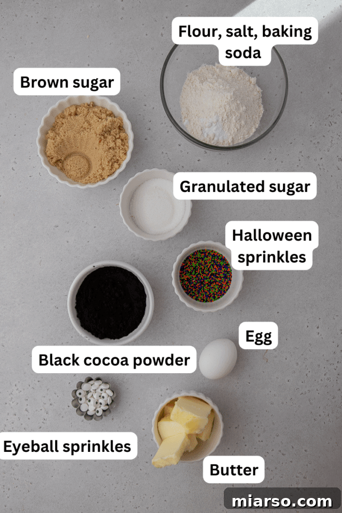 Various ingredients for black Halloween monster cookies laid out on a kitchen counter, including butter, sugars, flour, black cocoa, and sprinkles.