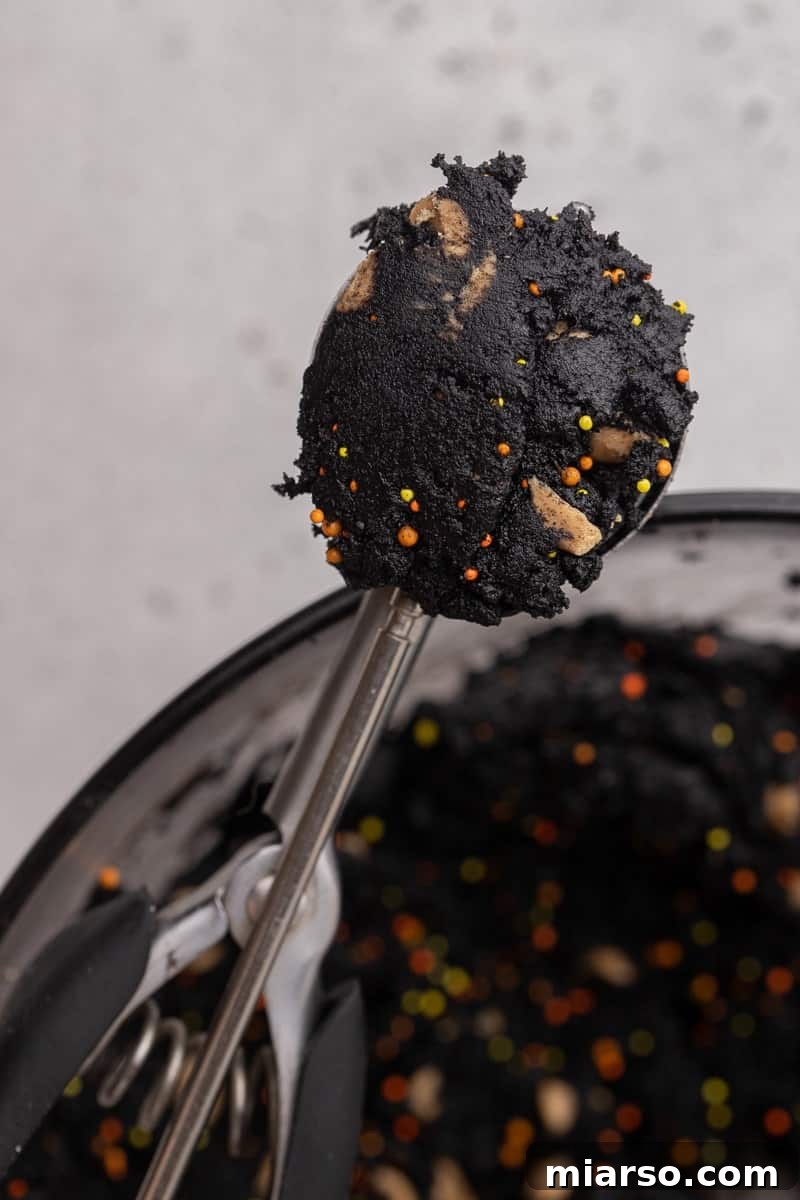 A cookie scoop filled with black cookie dough.