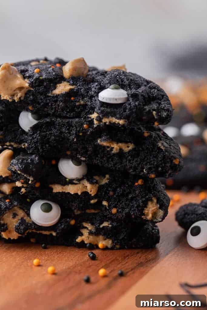Close-up of a stack of freshly baked black cocoa monster cookies with sprinkles and eyeballs.