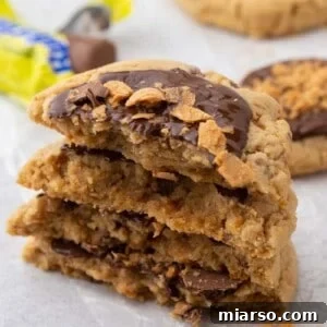 Stacked Crumbl Butterfinger peanut butter cookies showing soft chewy center with melted chocolate and crunchy Butterfinger pieces