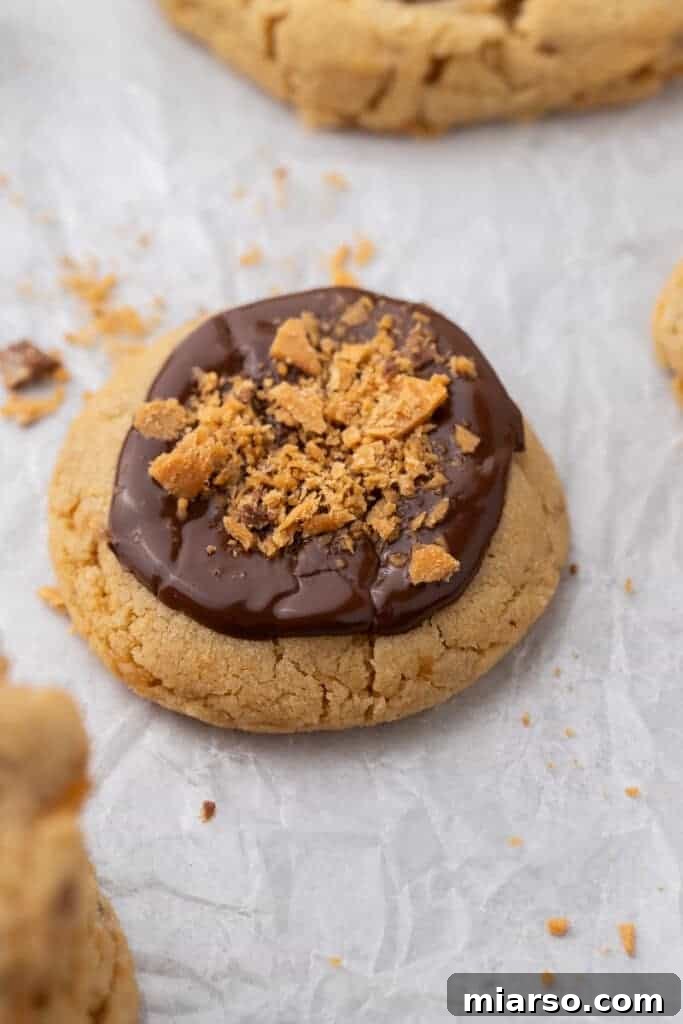 Ultimate Soft and Chewy Butterfinger Cookies 10 Close-up of Crumbl Butterfinger peanut butter cookie topped with melted chocolate and crushed Butterfinger pieces
