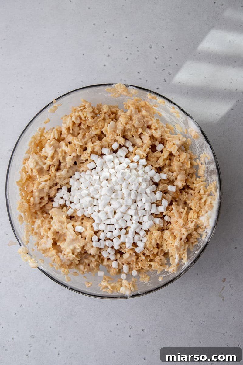 Rice Krispies cereal being folded into the warm, melted marshmallow mixture in a large bowl.