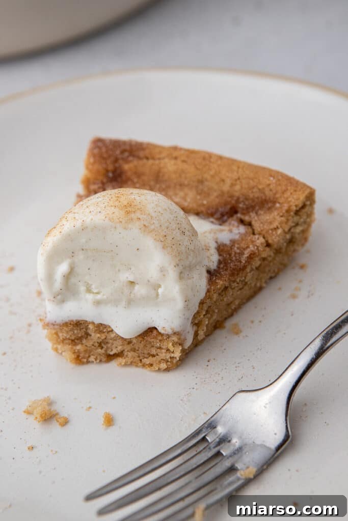 A large slice of Snickerdoodle pizookie in a cast iron skillet with ice cream and caramel drizzle, ready to be served.