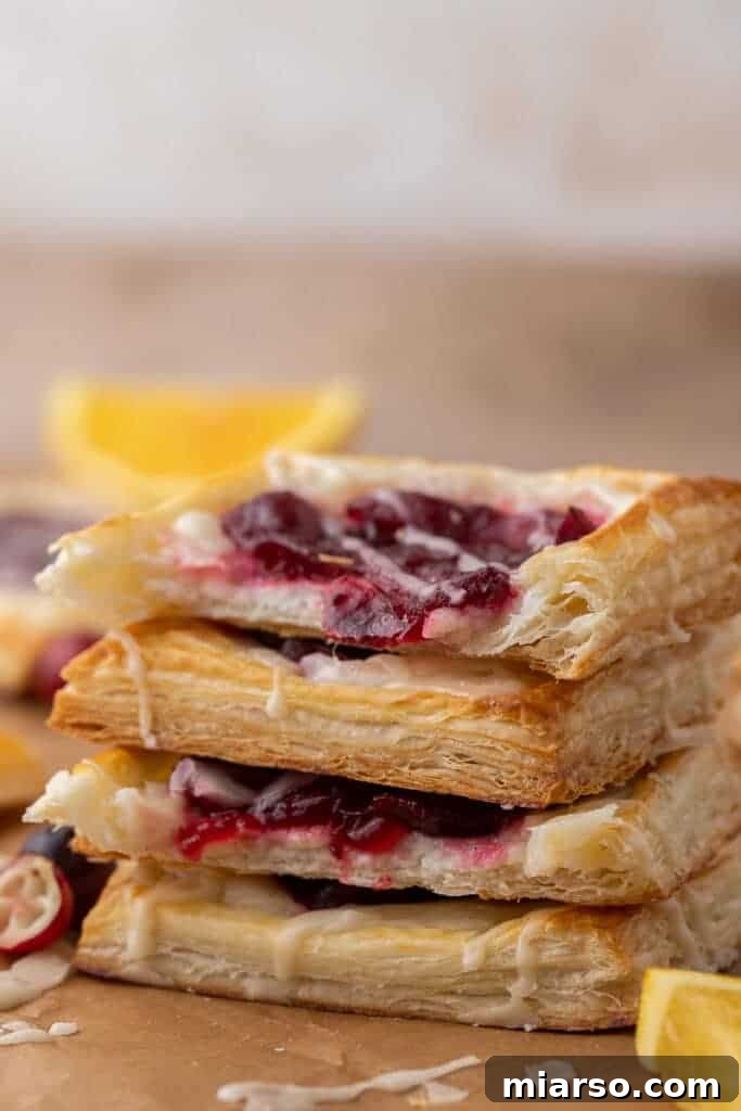 Cranberry Cheese Danish Revival 11 A stack of golden-brown Christmas cheese danishes, generously drizzled with white glaze, festive and inviting.