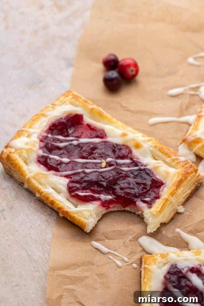 Cranberry Cheese Danish Revival 4 A close-up shot of a single cranberry sauce cheese danish with a bite taken out, showing the flaky puff pastry, creamy cheese filling, and vibrant cranberry sauce.