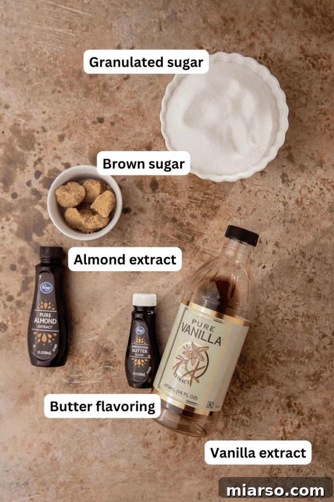 Various essential ingredients laid out neatly on a kitchen counter: brown sugar, granulated sugar, a measuring cup with water, and small bottles of vanilla, almond, and butter extracts.