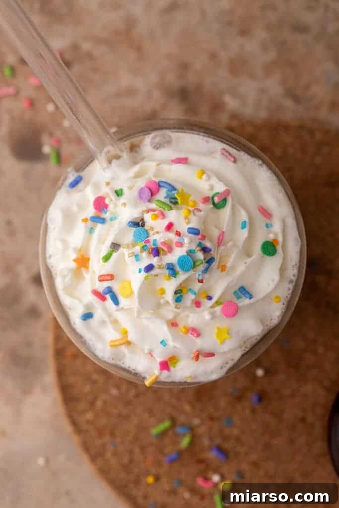 An overhead shot of an iced sugar cookie latte, topped with whipped cream and colorful festive sprinkles, capturing the holiday spirit.