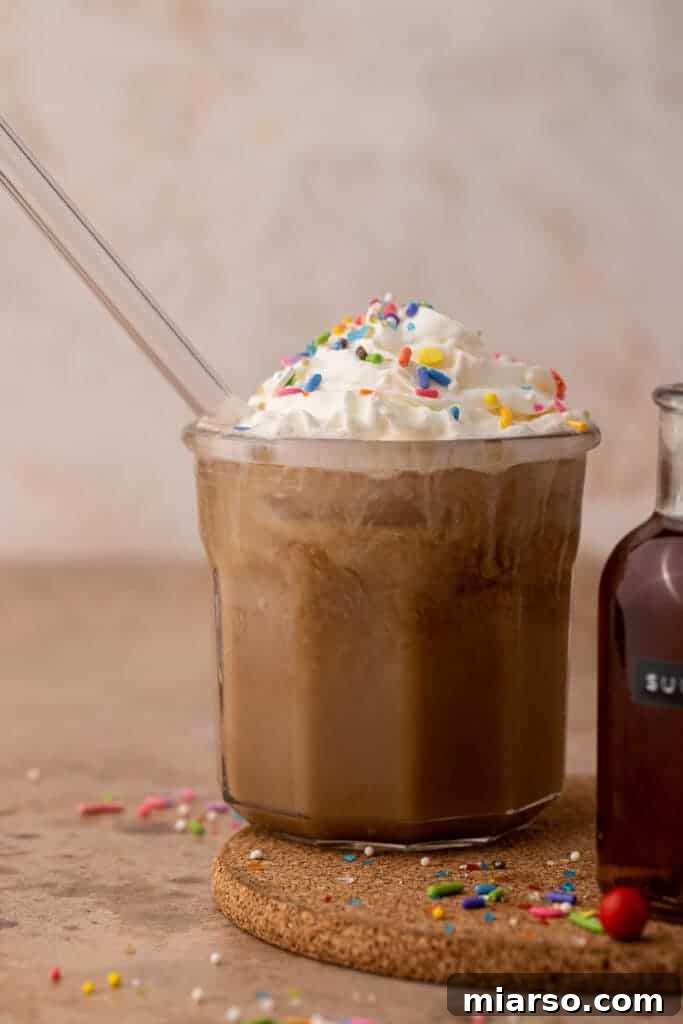 A refreshing cold brew sugar cookie drink, topped with a generous dollop of whipped cream and colorful sprinkles, served in a clear glass cup.