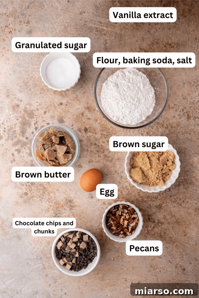 Overhead shot of labeled ingredients for cookies including flour, sugars, brown butter, chocolate, and pecans.
