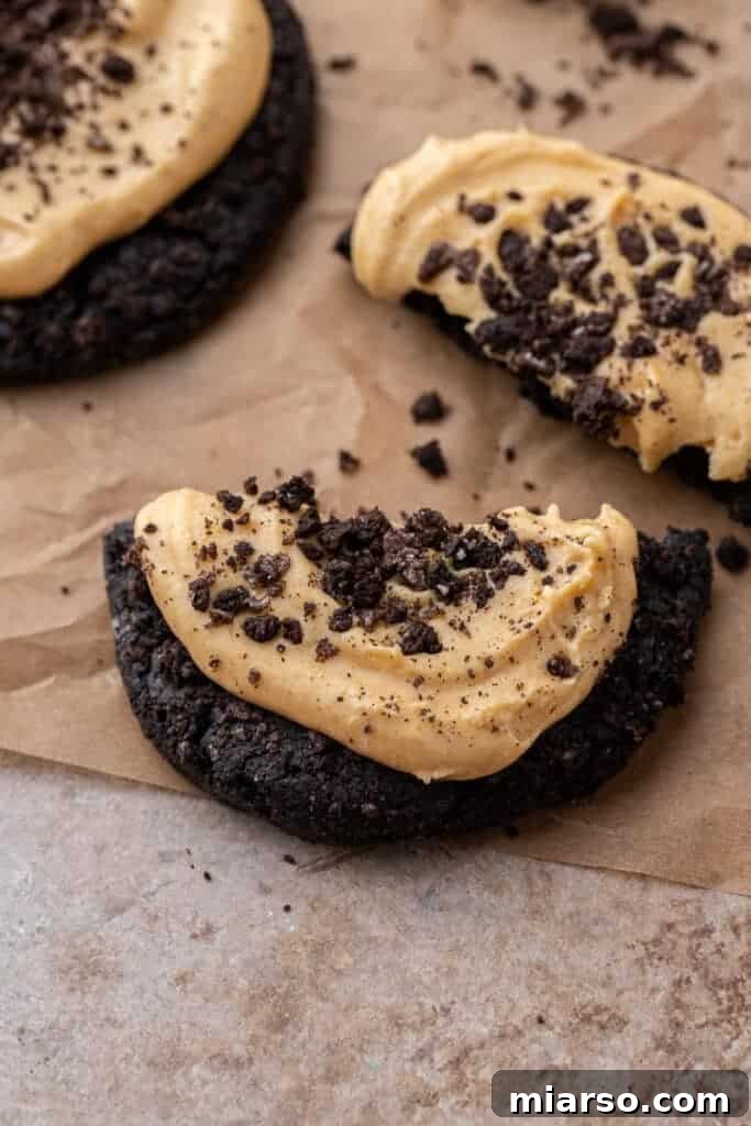 Decadent Crumbl Chocolate Pumpkin Cheesecake Cookies 4 Close-up of a dark black cocoa cookie with orange pumpkin cream cheese frosting, topped with Oreo crumbles