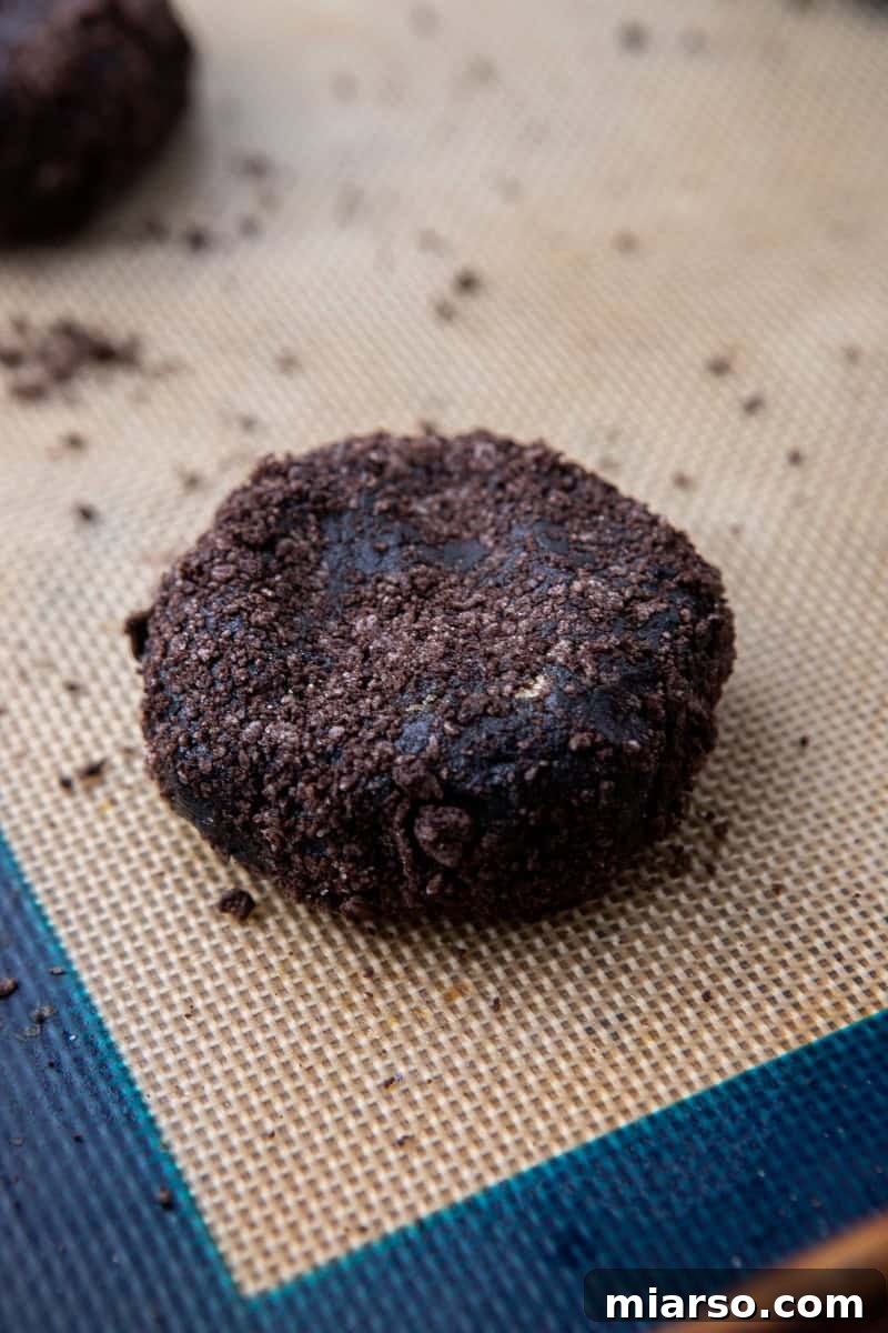 Decadent Crumbl Chocolate Pumpkin Cheesecake Cookies 9 Close-up of black cocoa cookie dough balls rolled in Oreo crumbs