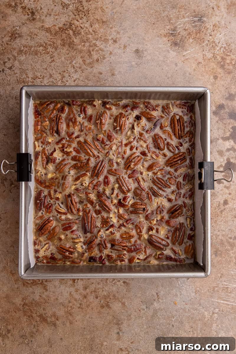 Pecan pie filling being poured over a golden shortbread crust in a baking pan.