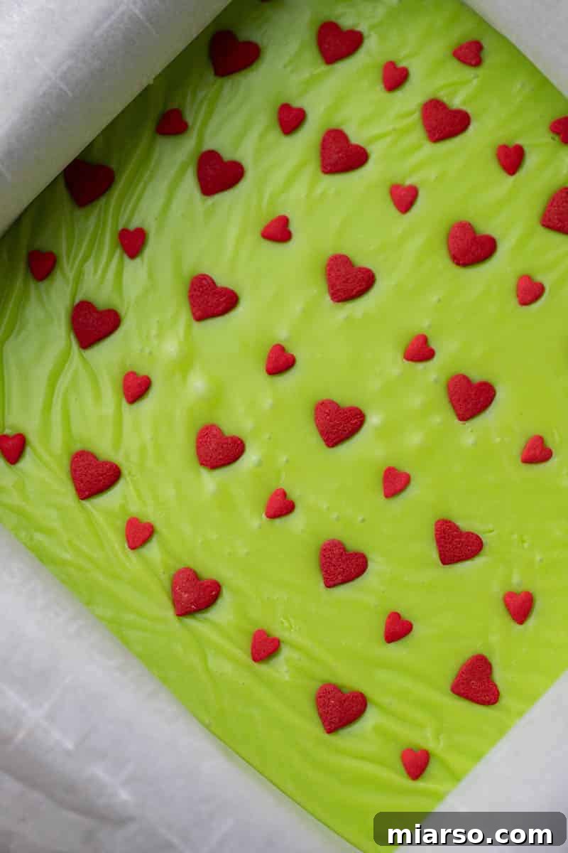 Grinch's Heart-Melting Fudge 6 Vibrant green Grinch fudge mixture poured into a parchment-lined pan, topped with red heart sprinkles.