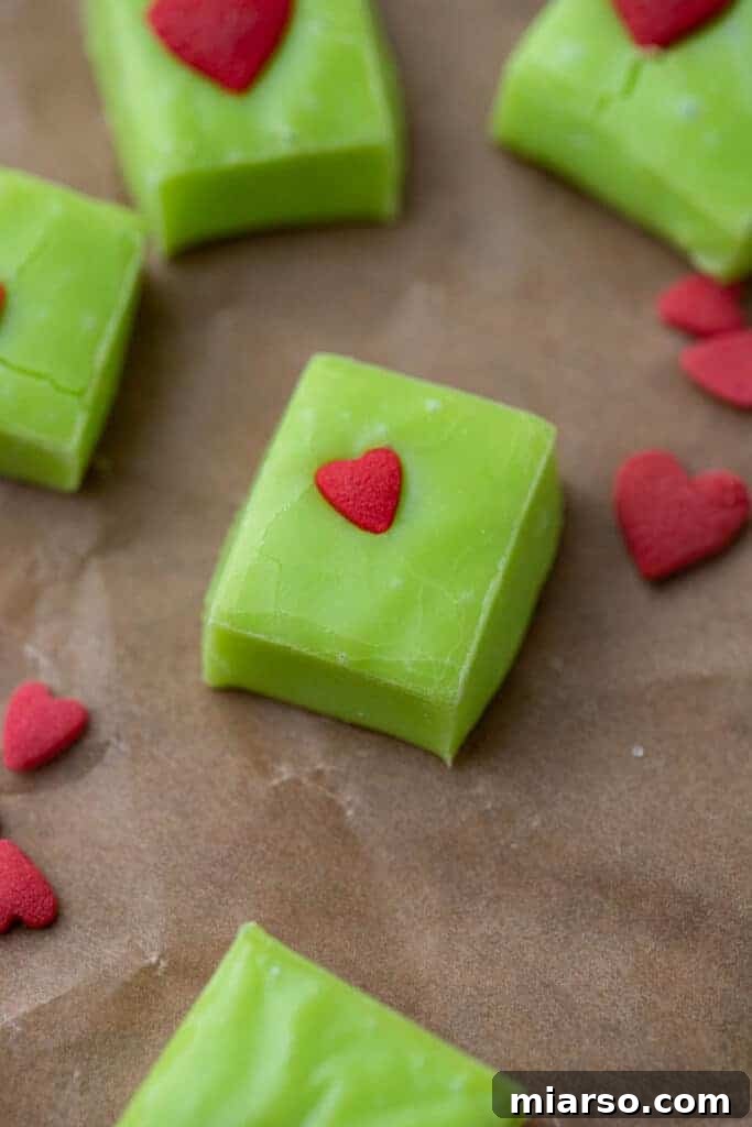 Grinch's Heart-Melting Fudge 8 A top-down shot of vibrant green Grinch fudge slices, perfectly square and adorned with red candy hearts, ready for a festive gathering.