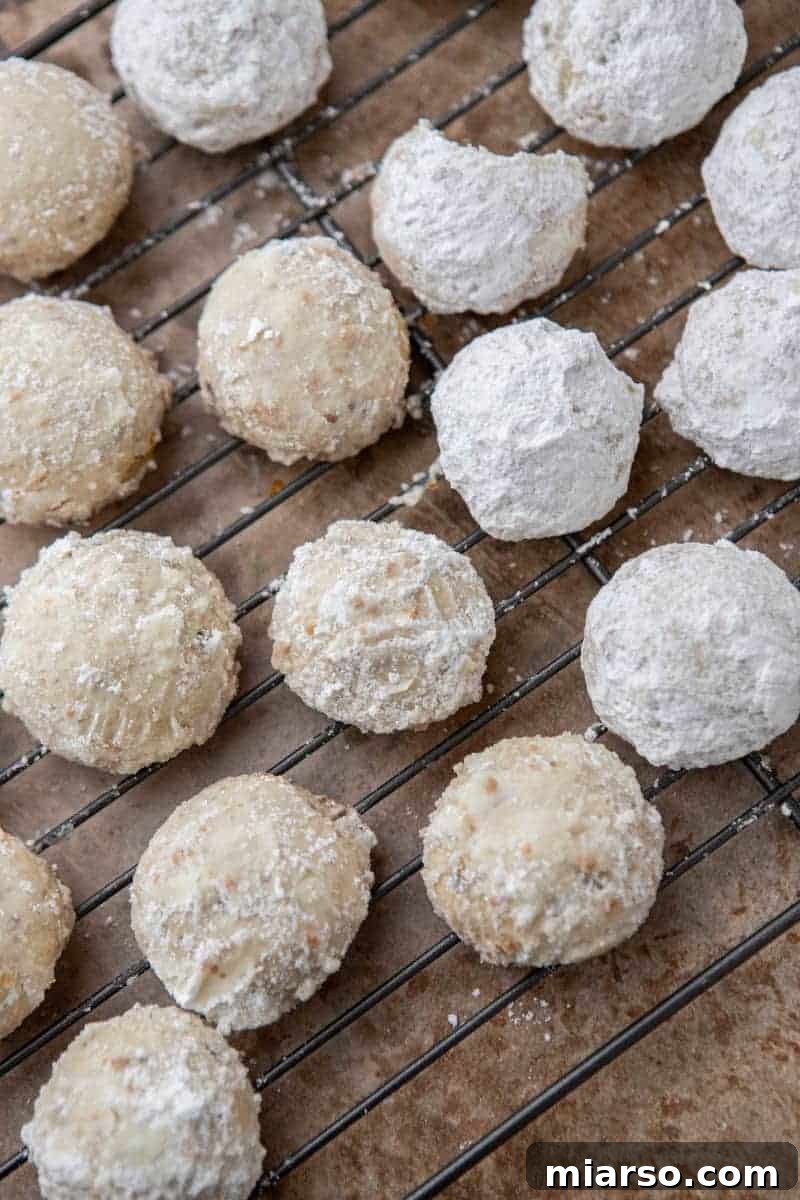 Melt-in-Your-Mouth Snowball Perfection 11 Snowball cookies cooling on a wire rack after their first powdered sugar coating, before the final dusting.