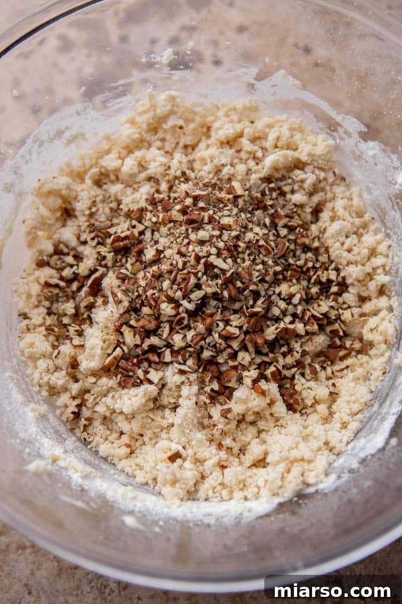 Melt-in-Your-Mouth Snowball Perfection 6 Cookie dough mixture forming in a bowl after adding flour and salt, illustrating the texture before adding nuts.